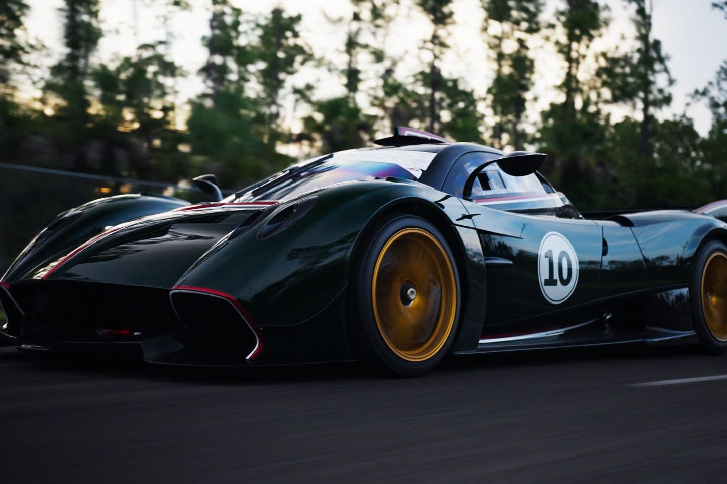 A dark green track-only hypercar with gold wheels at speed on the circuit at dusk, framed by Florida pines.